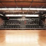 Empty theater stage with black chairs.