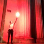 A man holding a torch in front of columns.
