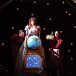 A woman holds a globe on stage.