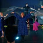 A group of performers dance with plastic.